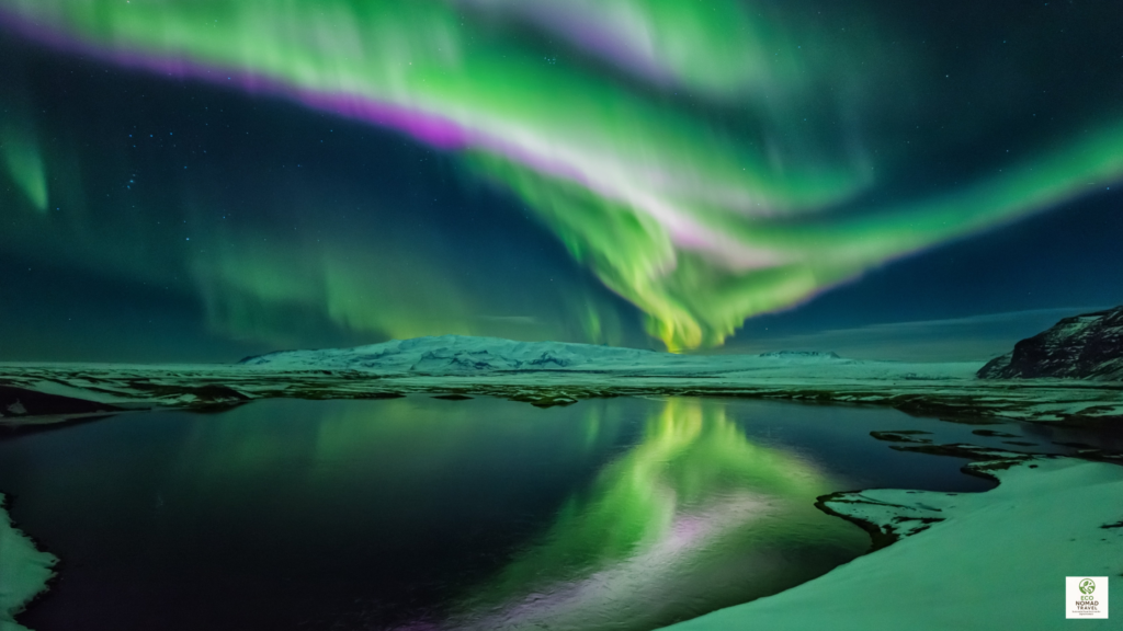 luxury in iceland with northern lights over calm water and a vivid green reflection beneath the aurora