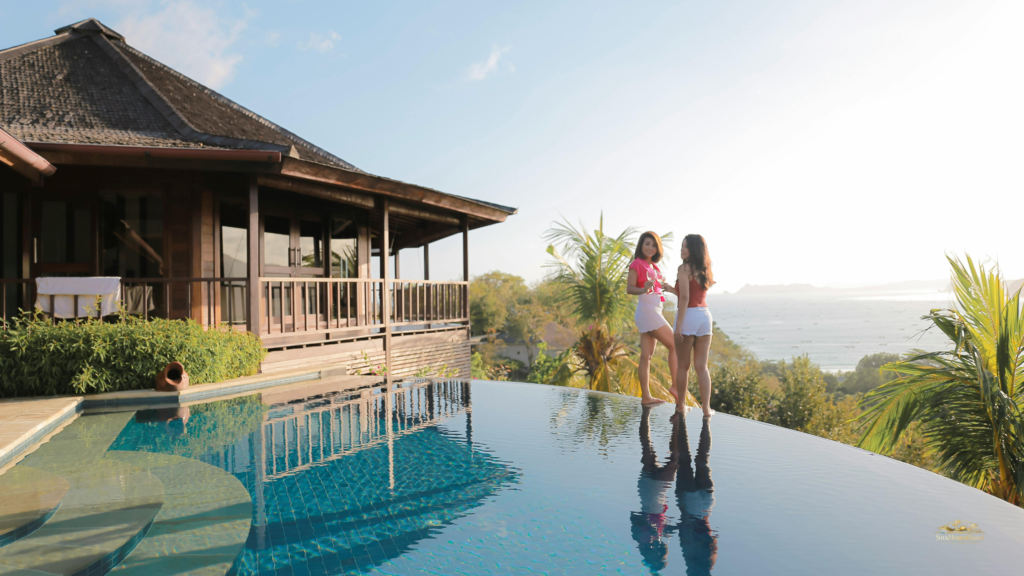 Two women standing by an infinity pool overlooking the ocean and lush trees—luxury in Bali.