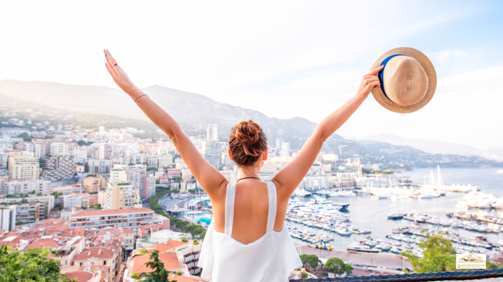 Woman with arms raised overlooking the Monaco skyline and harbor, capturing the feeling of luxury travel on the French Riviera.
