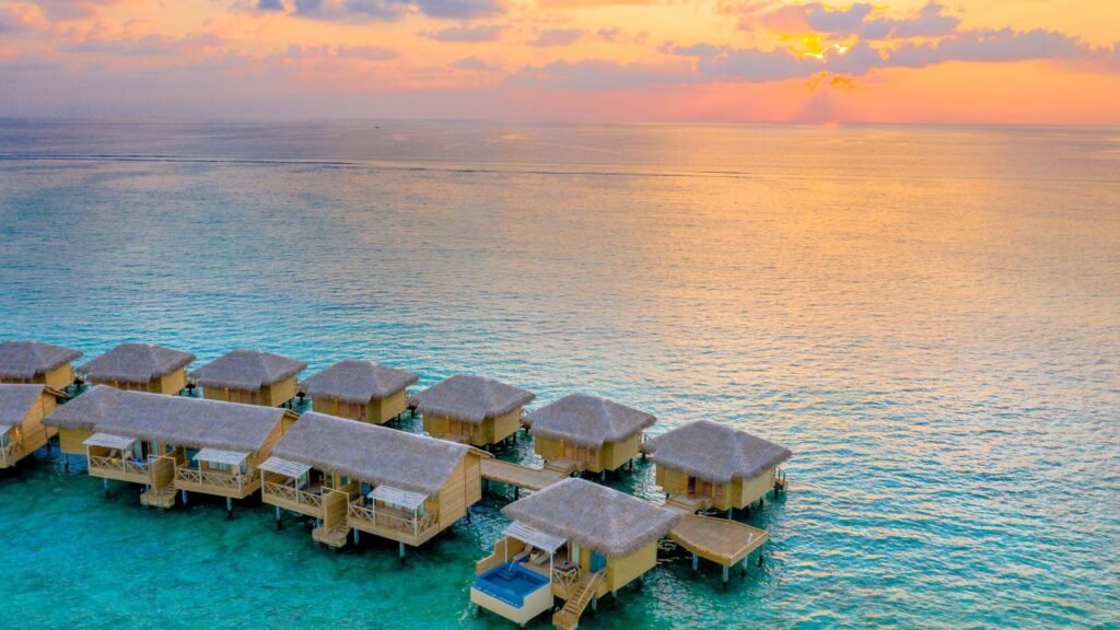 Aerial overwater villas at sunset for a honeymoon overwater villa vs beach villa guide