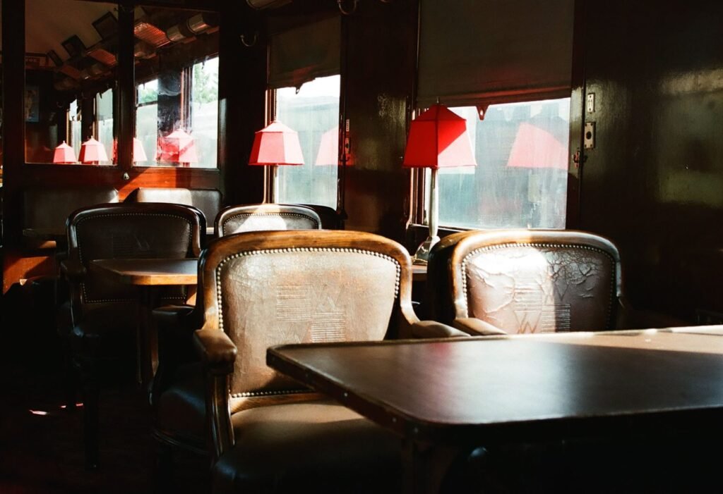 The interior of a vintage railway carriage with upholstered armchairs, a polished table and red-shaded table lamps