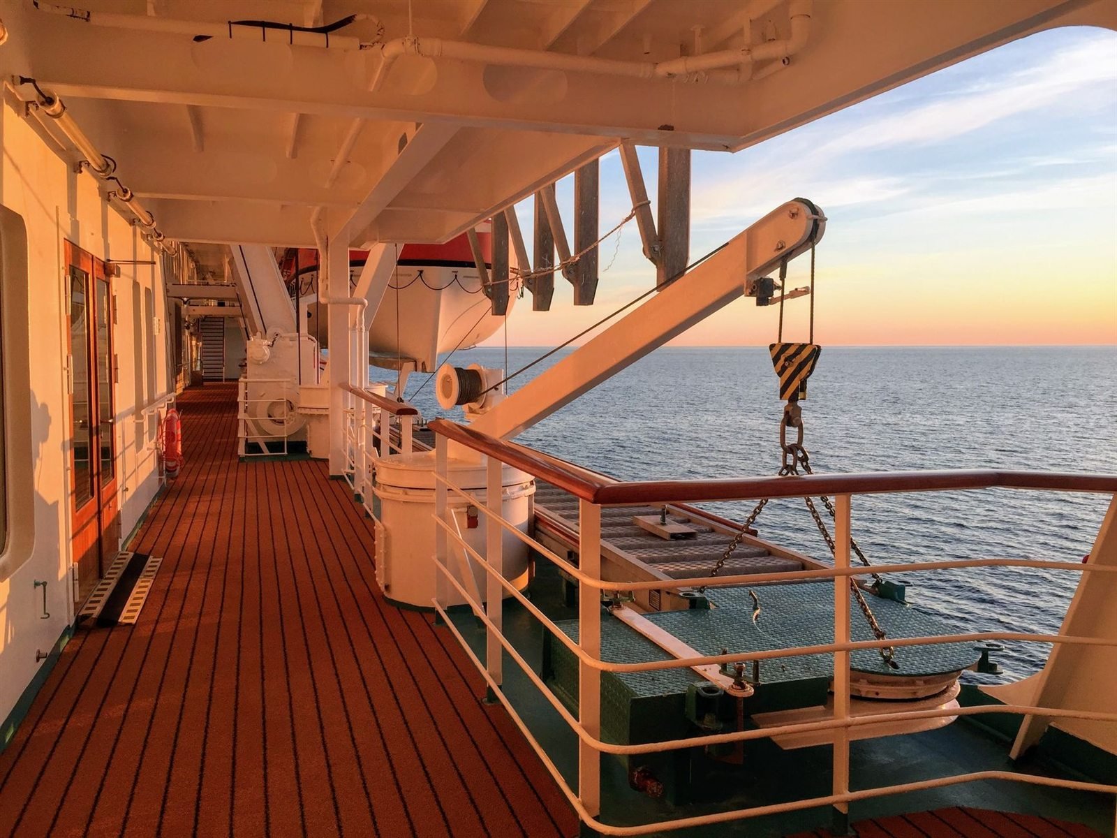 A covered wooden promenade deck on a ship looking out to sea at sunset